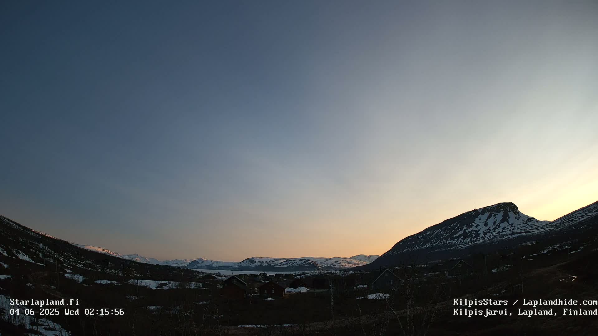 A twilight scene shows a small village nestled between snow-capped mountains under a clear, dusky sky.