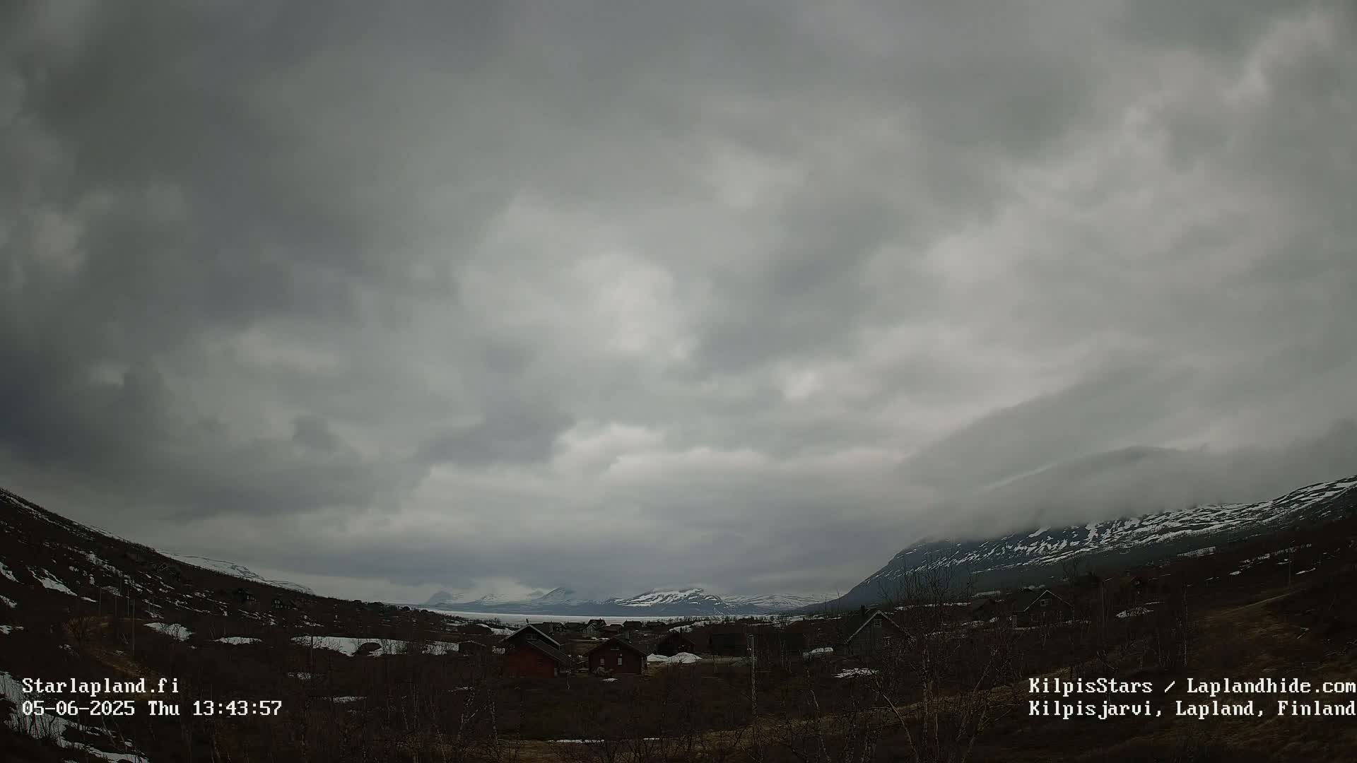 A small village nestled in a valley between snow-capped mountains under a cloudy, overcast sky.