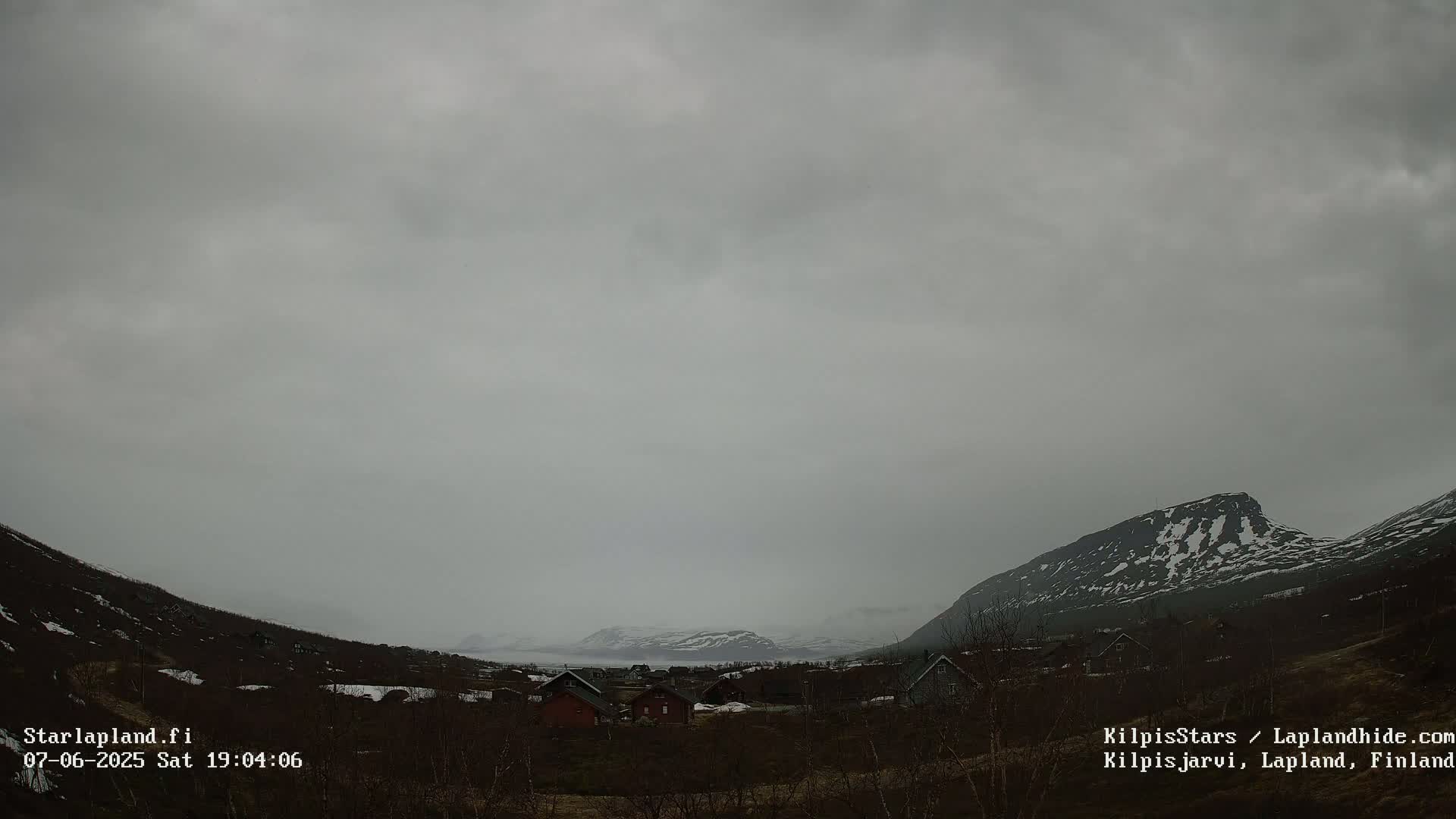 A small village nestled in a valley between snow-dusted mountains under an overcast sky.