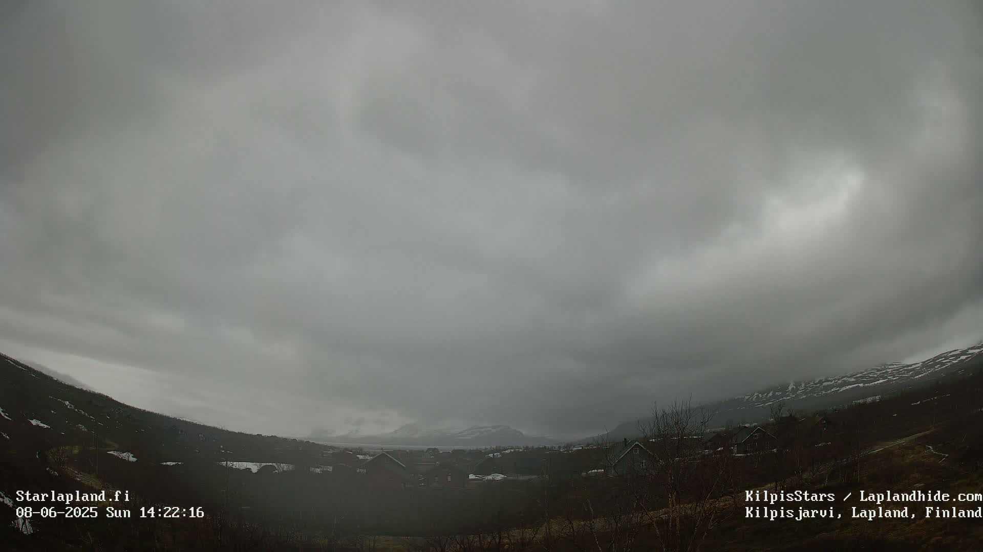 A small village nestled in a valley between snow-capped mountains under an overcast, gray sky.