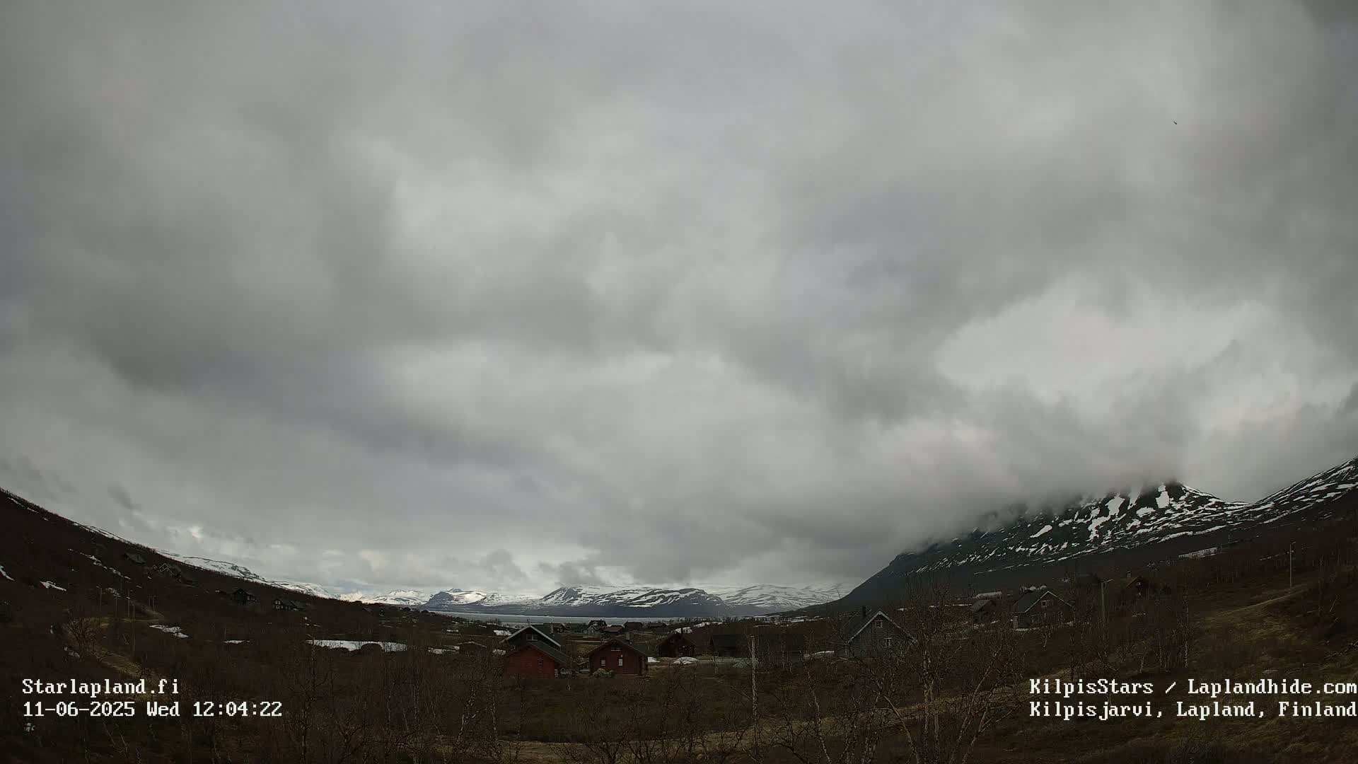 A cloudy, overcast day reveals a small village nestled between snow-capped mountains.