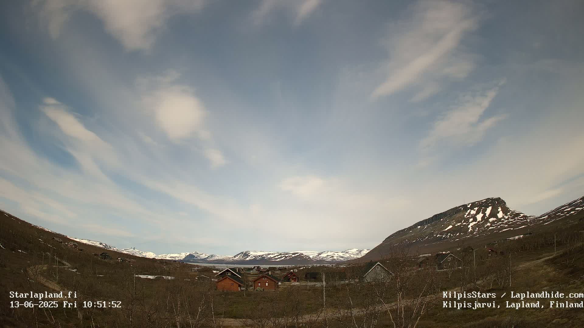 A small village nestled in a valley between snow-capped mountains under a partly cloudy sky.