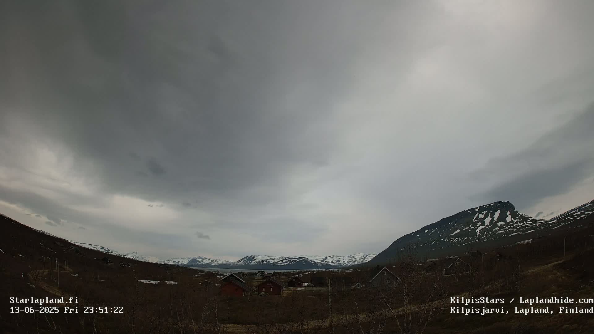 A small village nestled in a valley between snow-capped mountains under a heavily overcast sky.