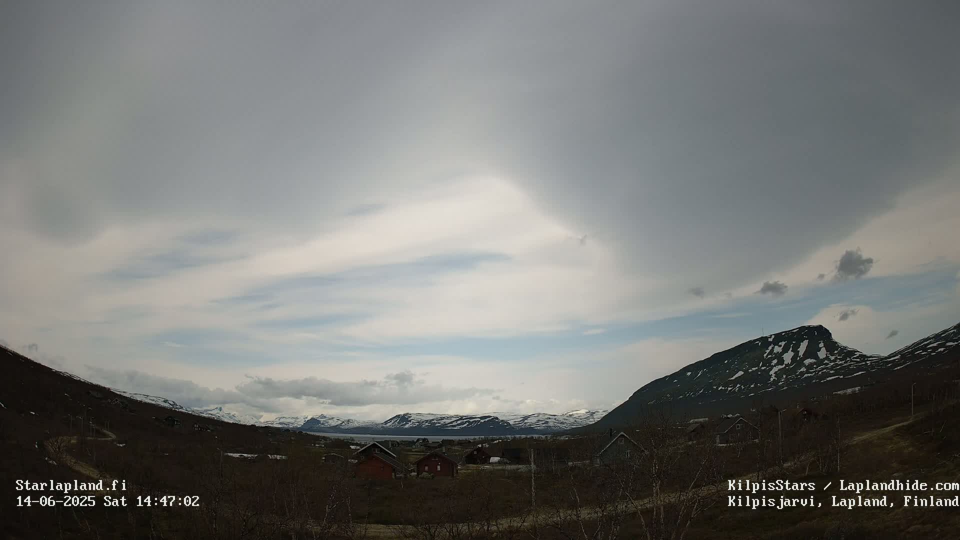 A mostly cloudy sky hangs over a sparsely populated valley nestled between snow-capped mountains.