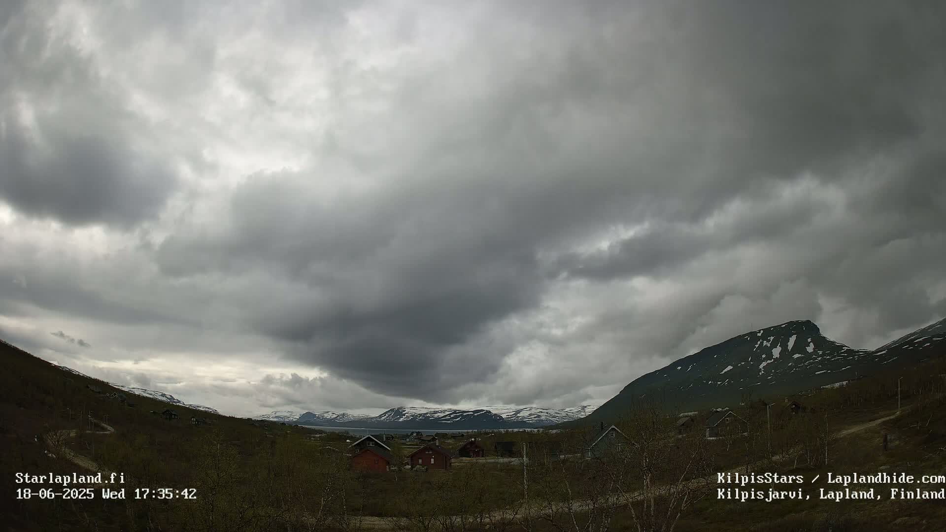 A small village nestled in a valley between snow-capped mountains under a heavily overcast sky.
