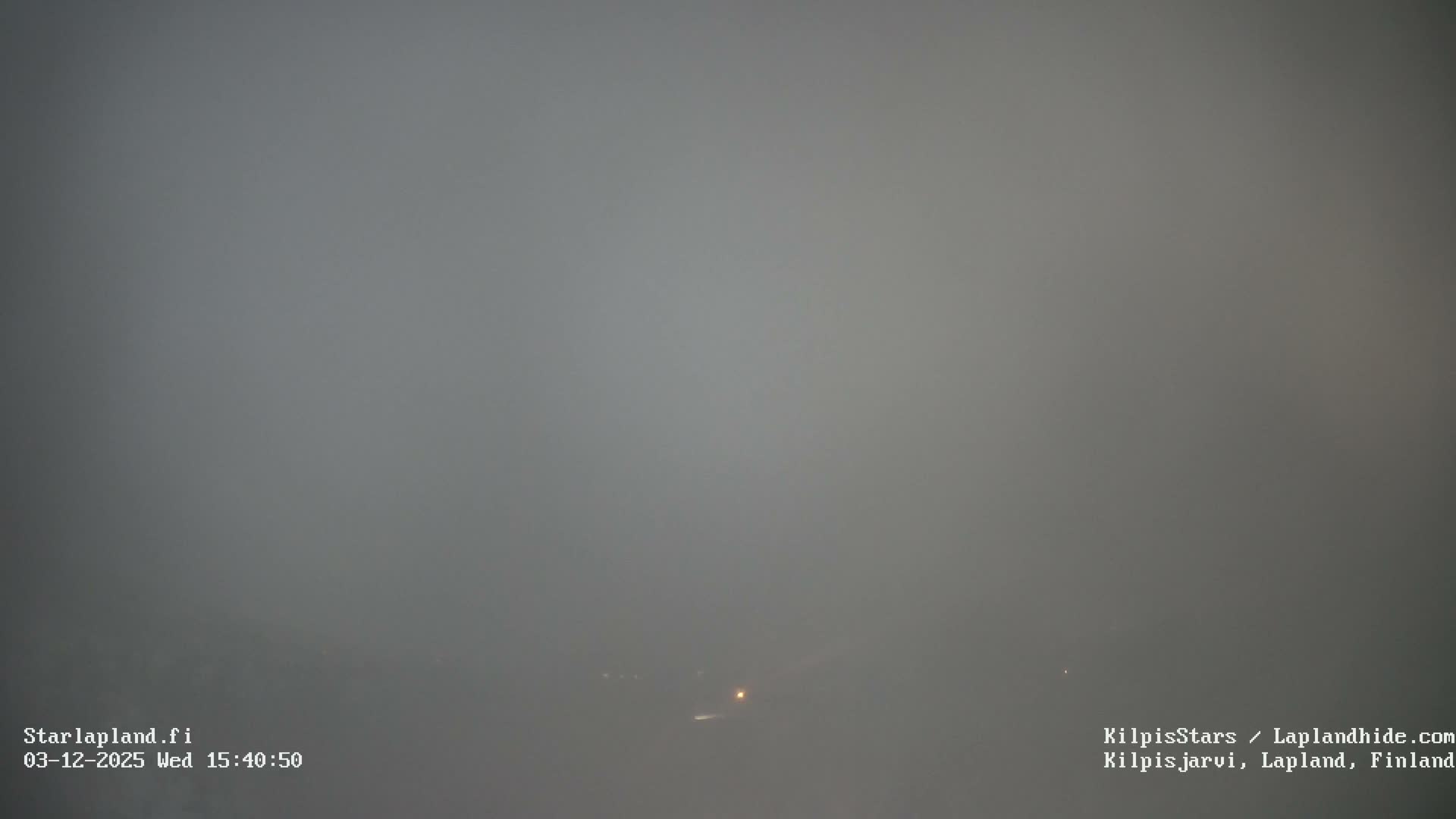 The image shows an outdoor scene almost entirely obscured by dense gray fog or heavy overcast conditions, with only a few faint lights visible near the horizon.