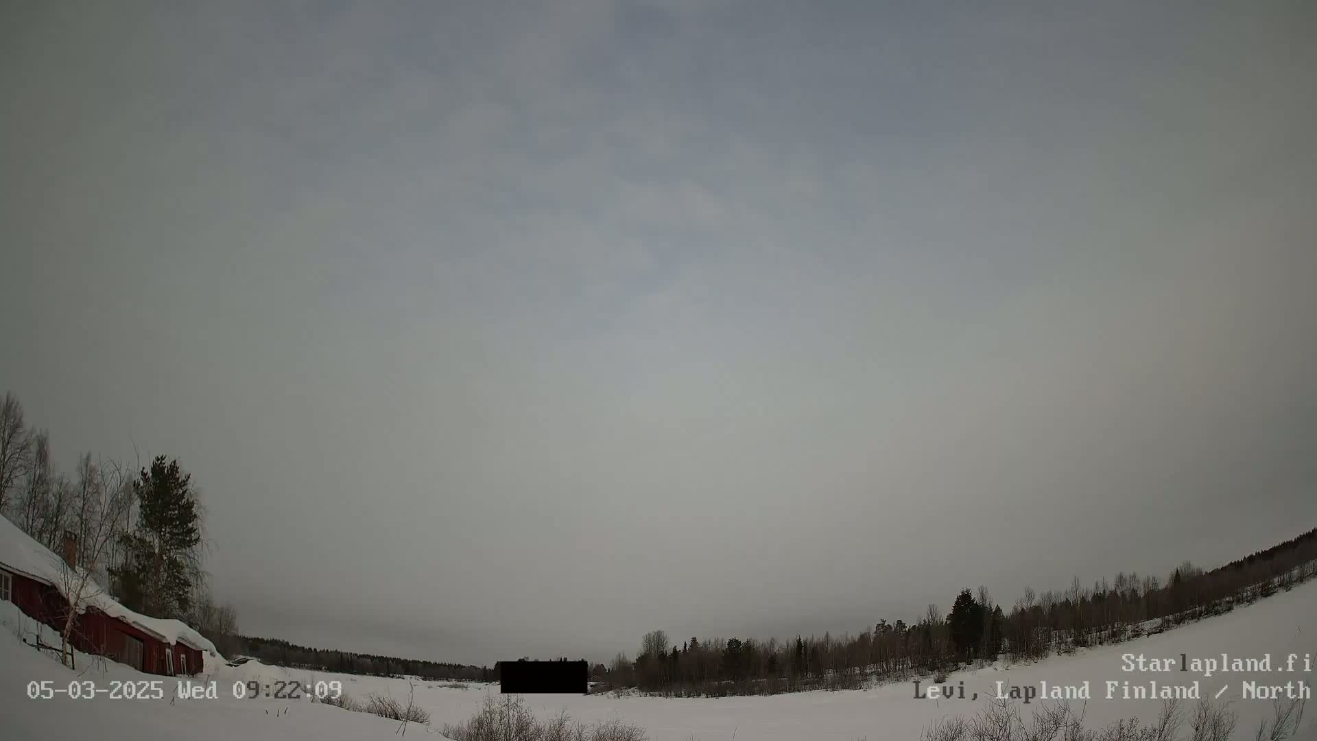 A snow-covered landscape with a red building and bare trees under an overcast sky.