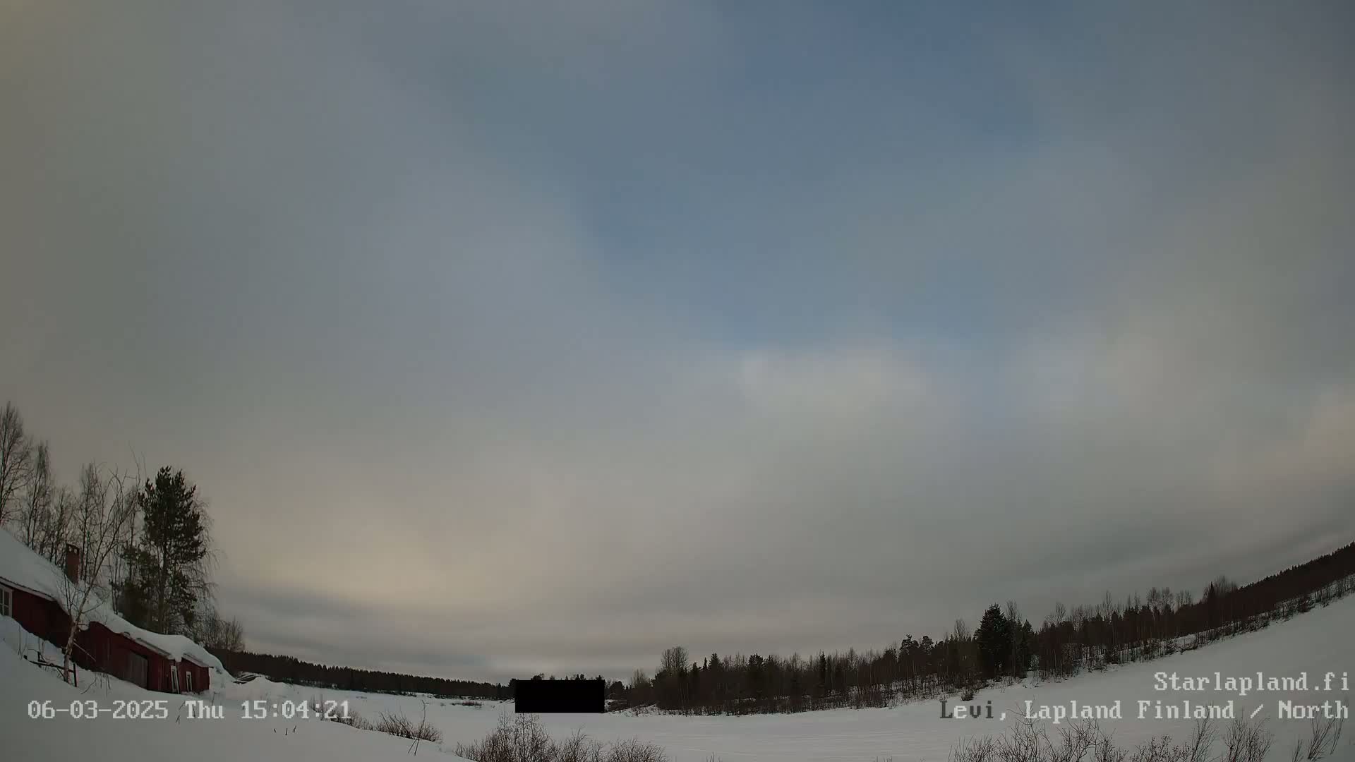A snow-covered landscape with a red building and trees under a mostly cloudy, pale sky.