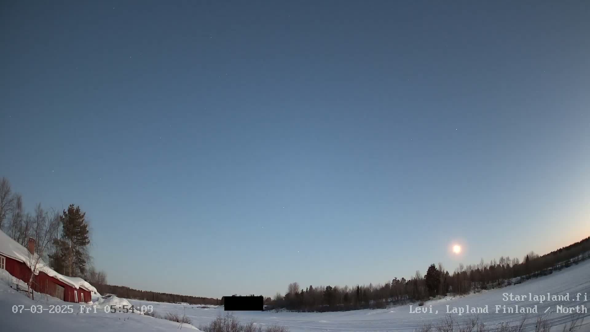 A snow-covered landscape with a red building and a few trees is visible under a clear twilight sky with a bright moon.