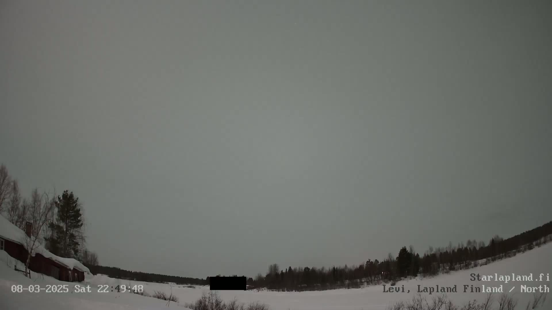 A snow-covered landscape with a dark building and trees under a light gray sky.