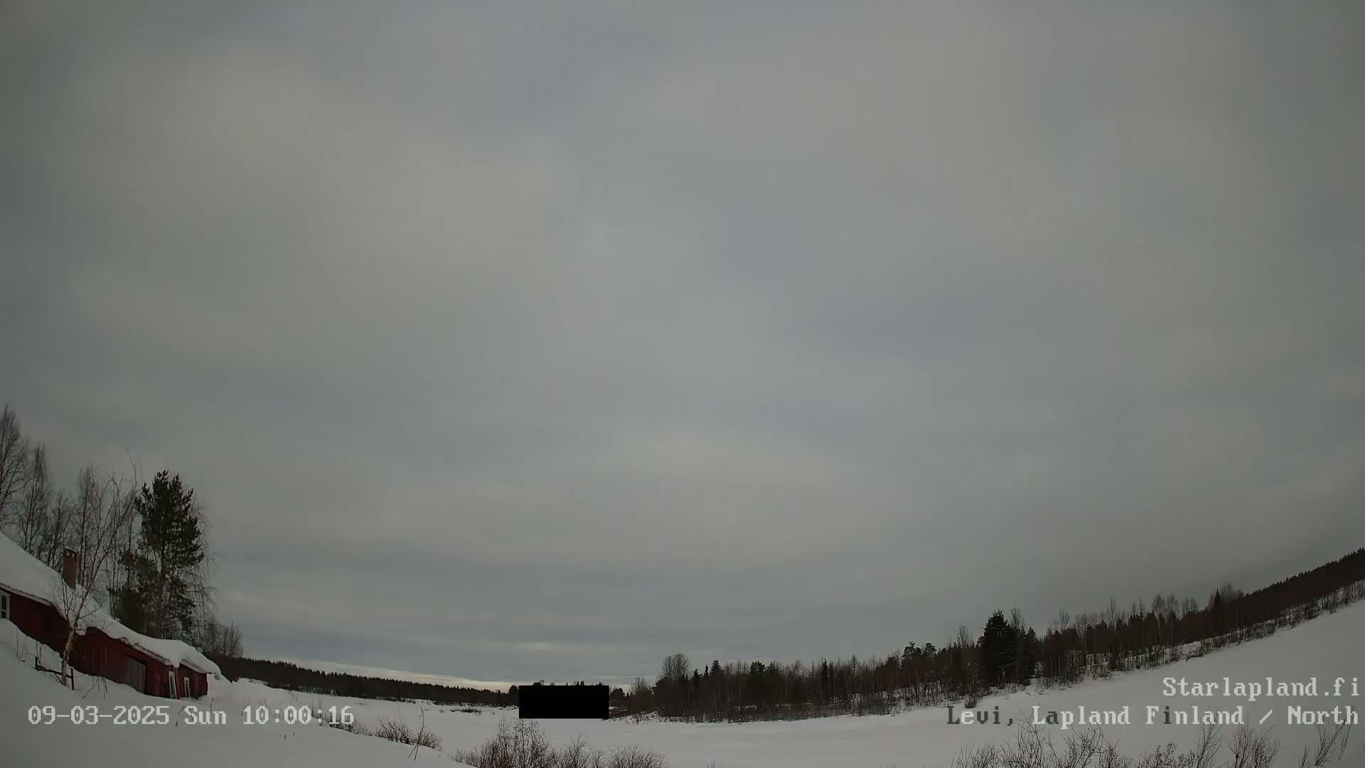 A snow-covered landscape with a red building and dark trees under an overcast sky.