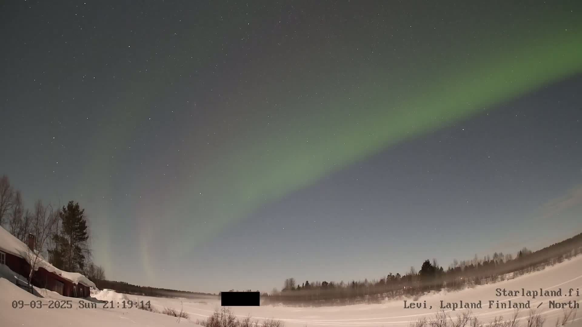A nighttime snow-covered landscape displays a vibrant aurora borealis under a starry sky.