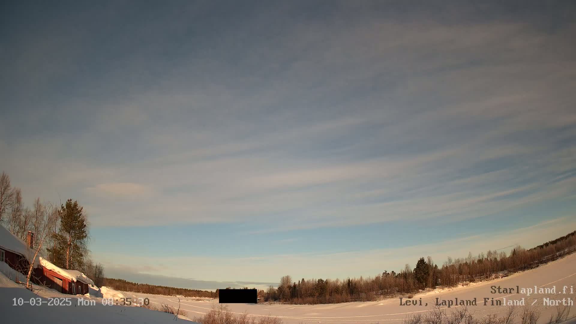 A snow-covered landscape with a red building and thin, wispy clouds in a pale blue sky.