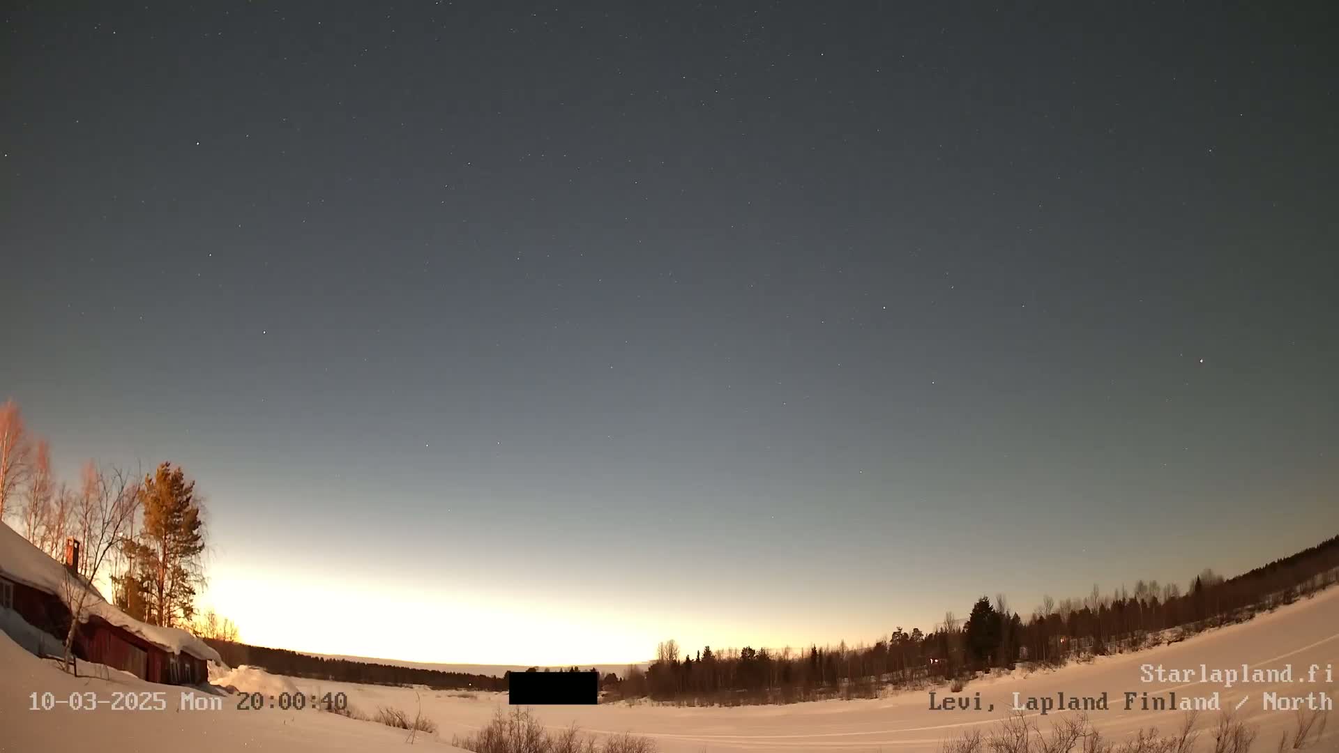 A snow-covered landscape with a few trees and a building is visible under a twilight sky dotted with stars.