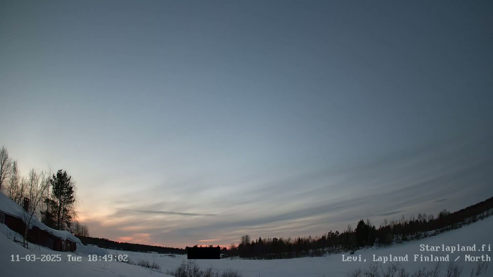 A red building is partially visible in the bottom left corner of a snowy landscape at twilight under a mostly clear sky with faint clouds.
