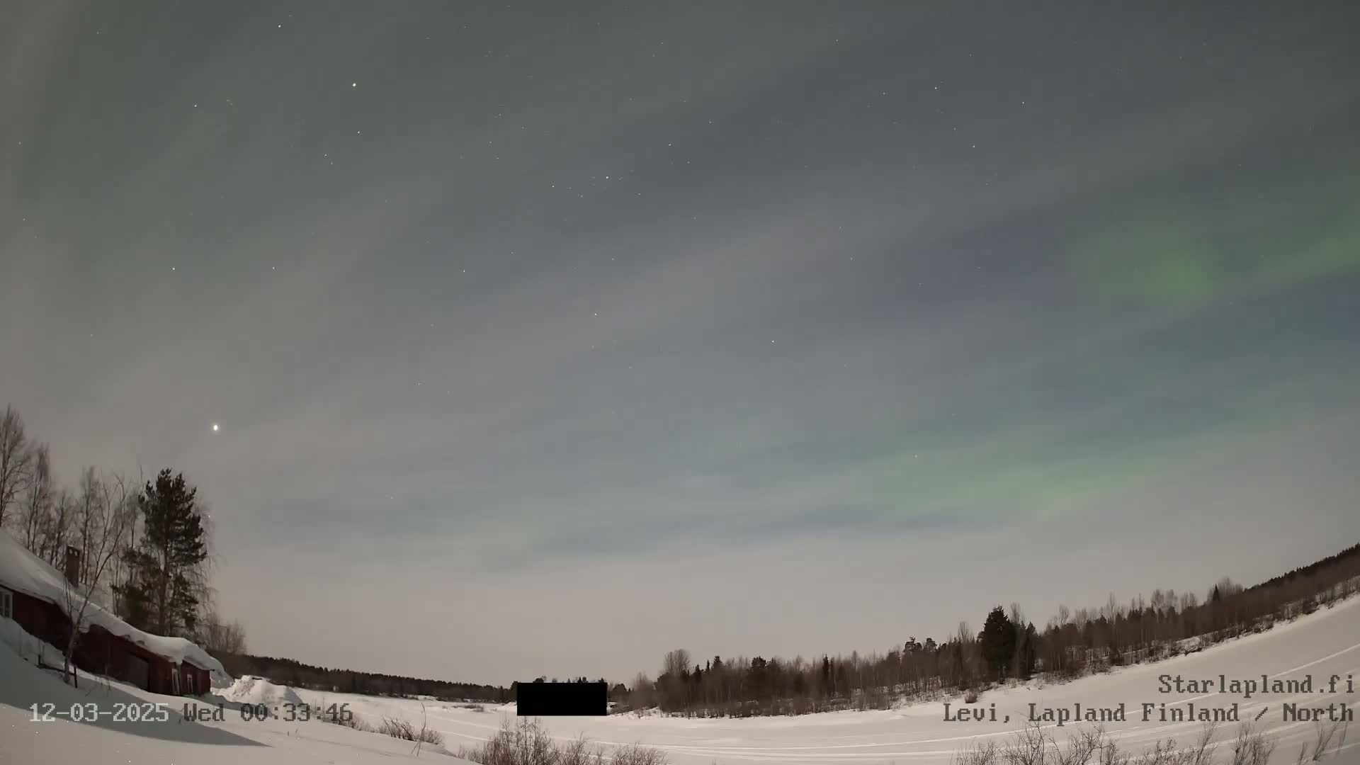 A snow-covered landscape under a night sky displaying a faint aurora borealis, with a few stars and a building visible in the foreground.