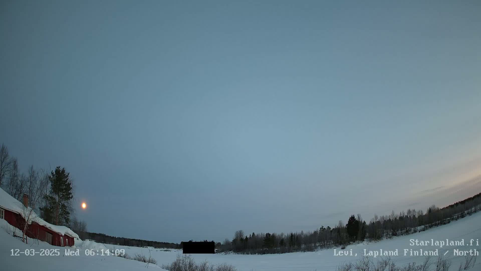 A low-lying sun is visible in a pale blue, twilight sky over a snow-covered landscape featuring a red house, leafless trees, and a dark, rectangular object in the middle distance.