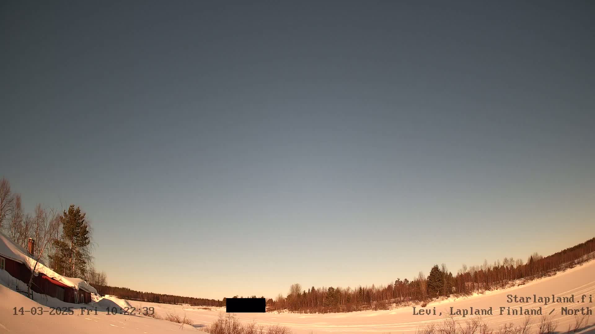 A snow-covered landscape with a red building and trees under a clear, twilight sky.