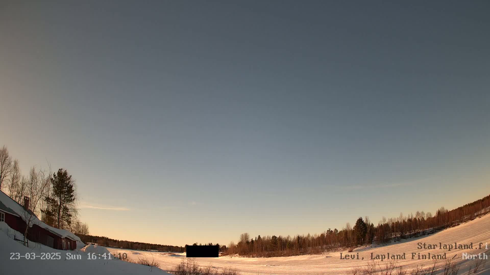 A snow-covered landscape with a red building and trees under a clear, twilight sky.