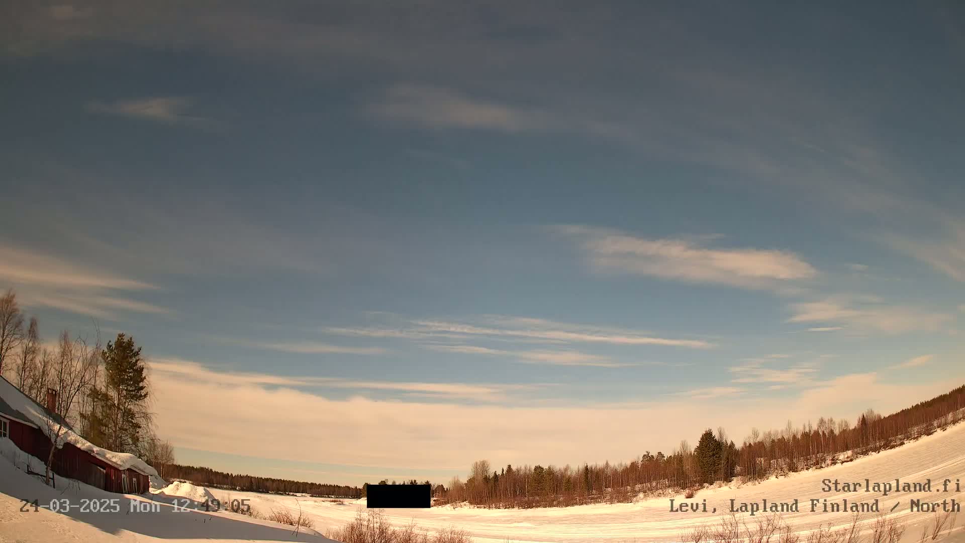 A snow-covered landscape with a red building and leafless trees under a mostly clear sky with wispy cirrus clouds.
