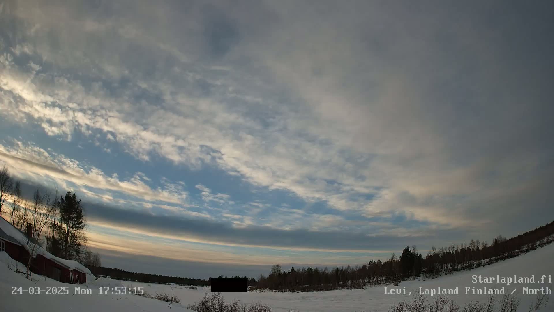 A mostly cloudy, twilight sky over a snow-covered landscape with a red house and a line of trees in the distance.