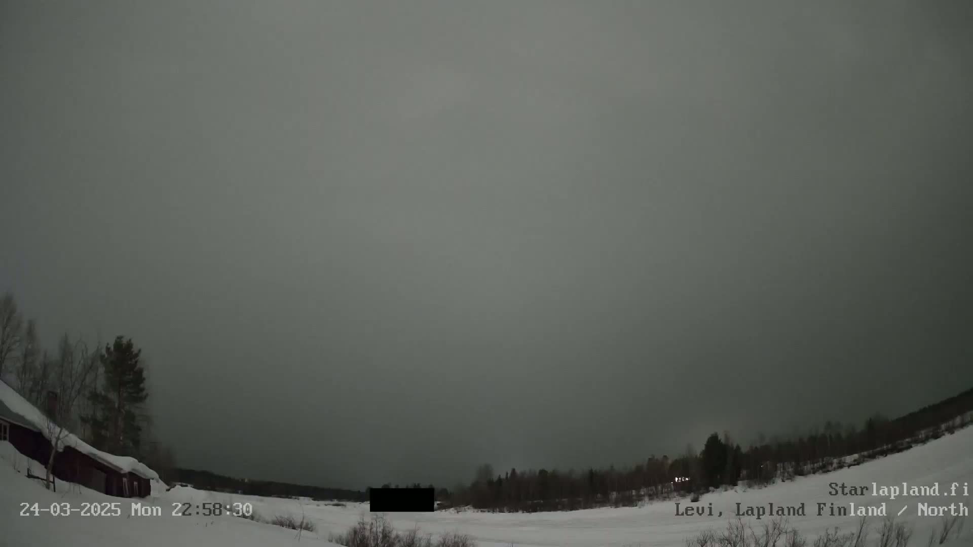 A snow-covered landscape with a dark, overcast sky is visible at dusk, showing a few trees and buildings in the distance.