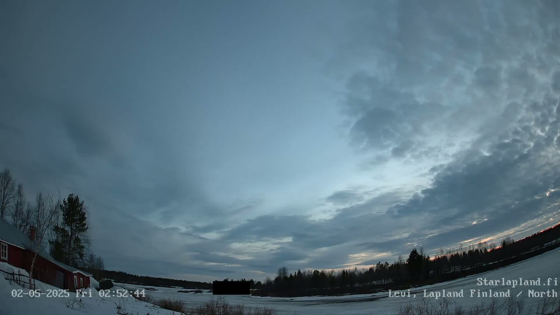 A snow-covered landscape with a red building and trees under a mostly cloudy, twilight sky.