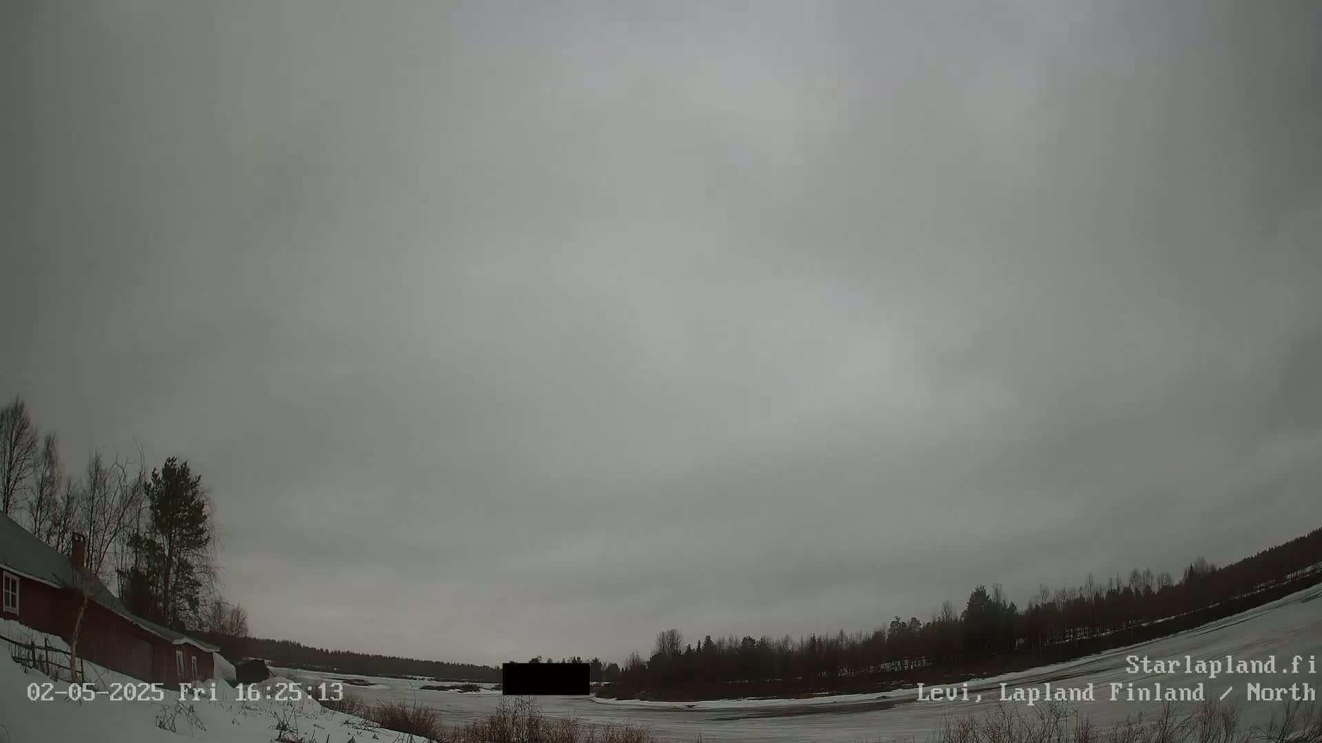 A snow-covered landscape under an overcast sky shows a red building to the left and a line of trees in the distance.