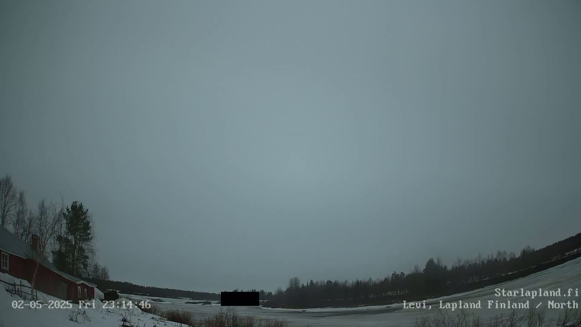 A snow-covered landscape with a red building and trees under an overcast sky.