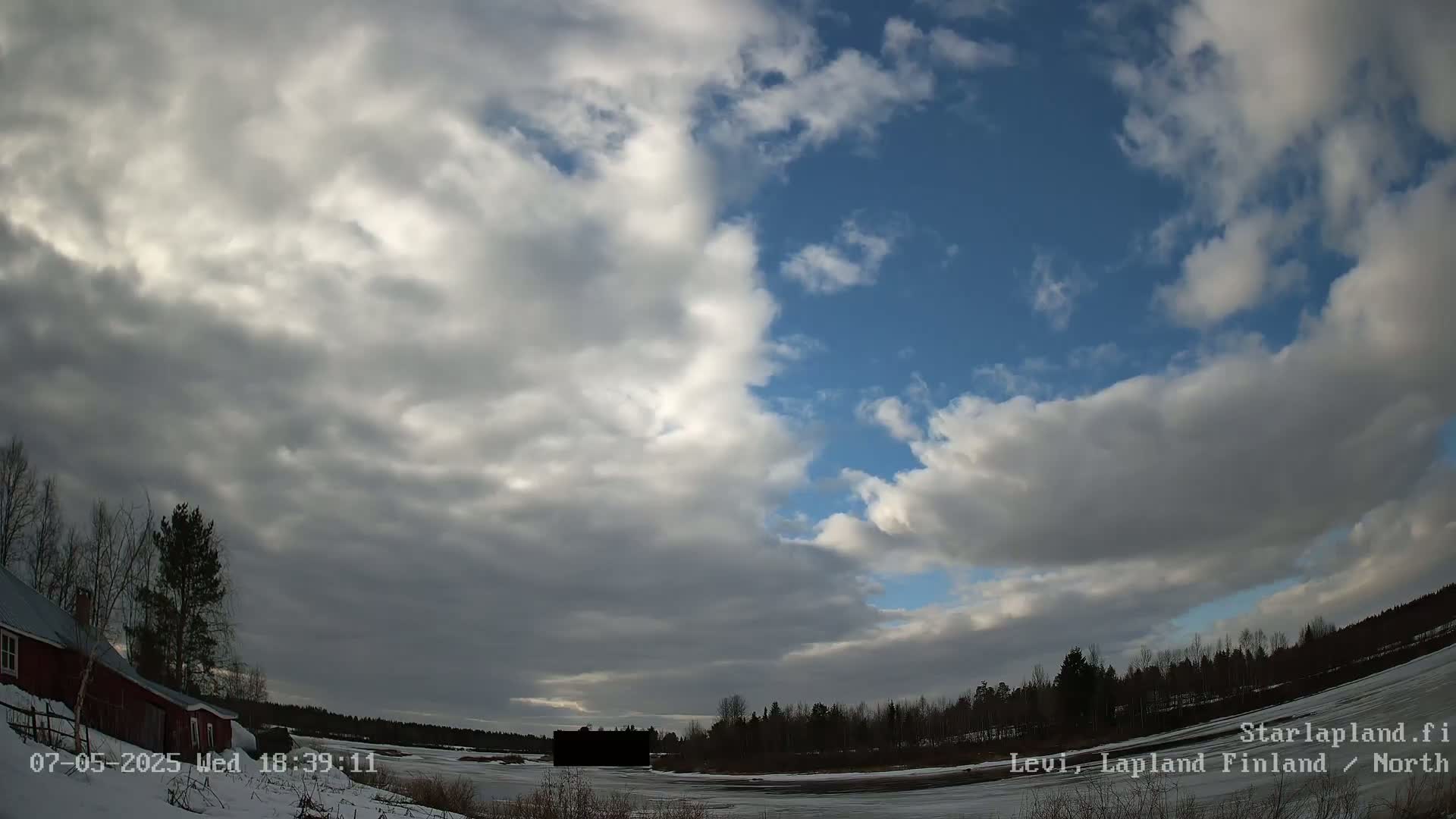 A partly cloudy sky over a snow-covered landscape with a red building and trees, under partly cloudy skies.