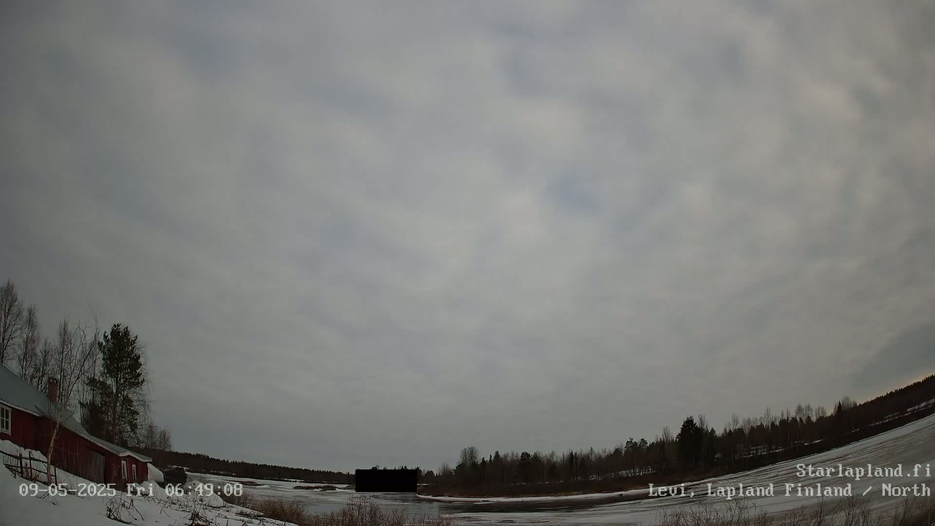 A mostly cloudy sky over a snow-covered landscape with a red barn and some trees, under overcast conditions.