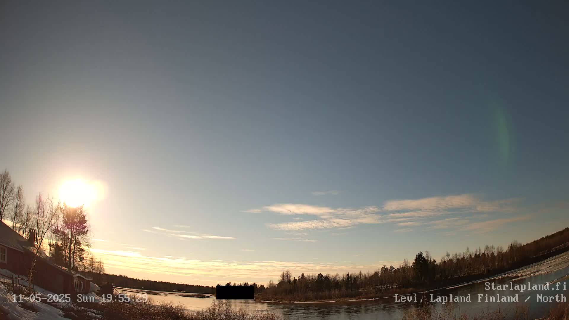 A mostly clear, sunset sky over a snow-covered landscape with a river, bare trees, and a few buildings.