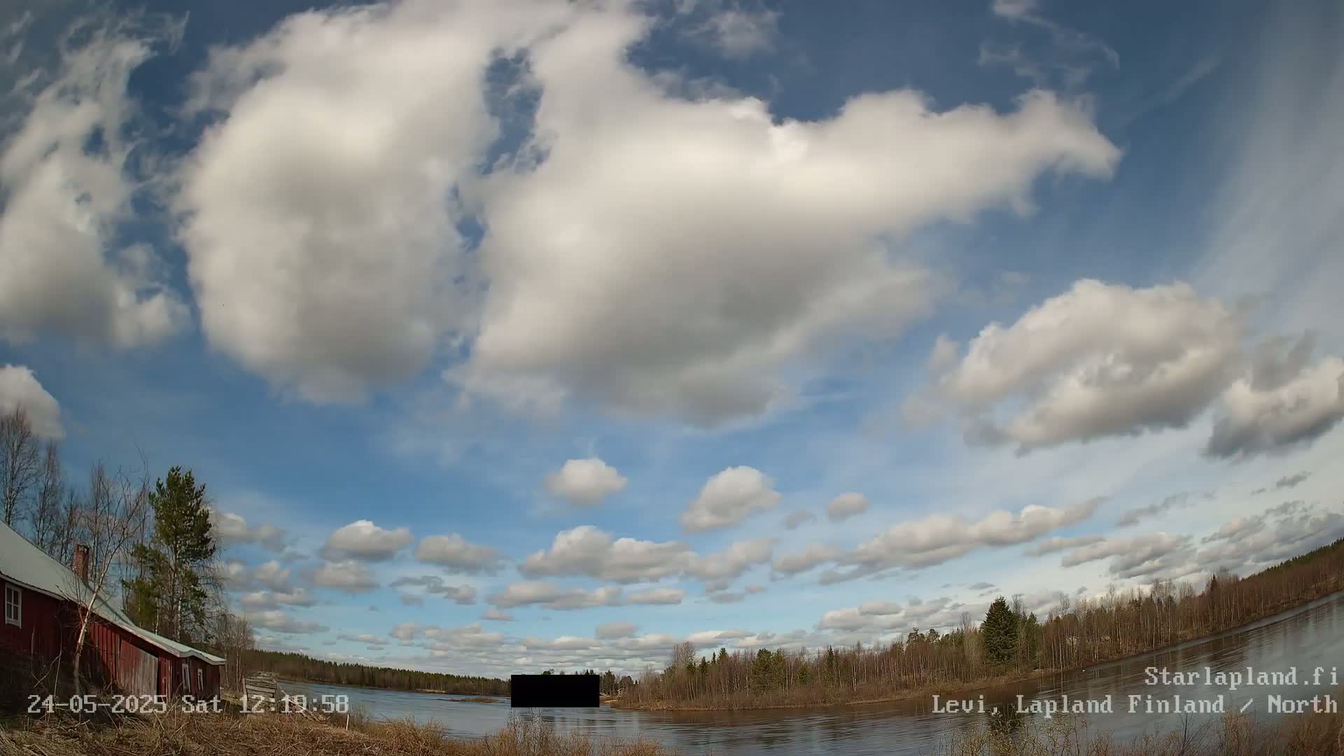 A partly cloudy sky over a calm river, with a red house and trees visible on the left bank.