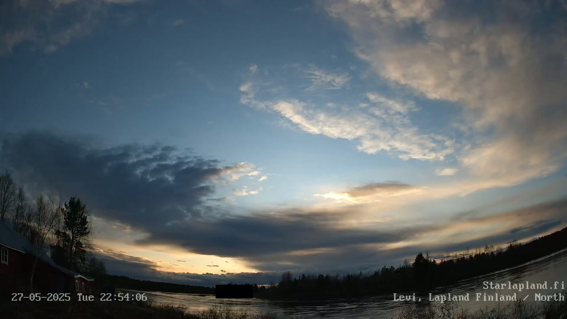 A twilight sky with partly cloudy conditions over a calm river, bordered by dark trees and a red house.