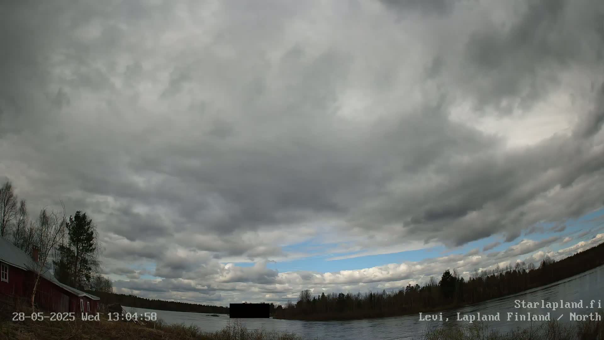 A mostly cloudy sky over a calm river, with a red building and trees visible on the left bank.