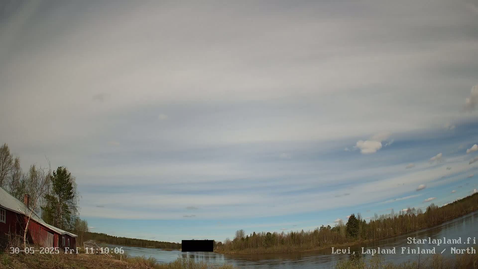 A mostly cloudy sky over a calm river, with a red house and trees visible on one bank.