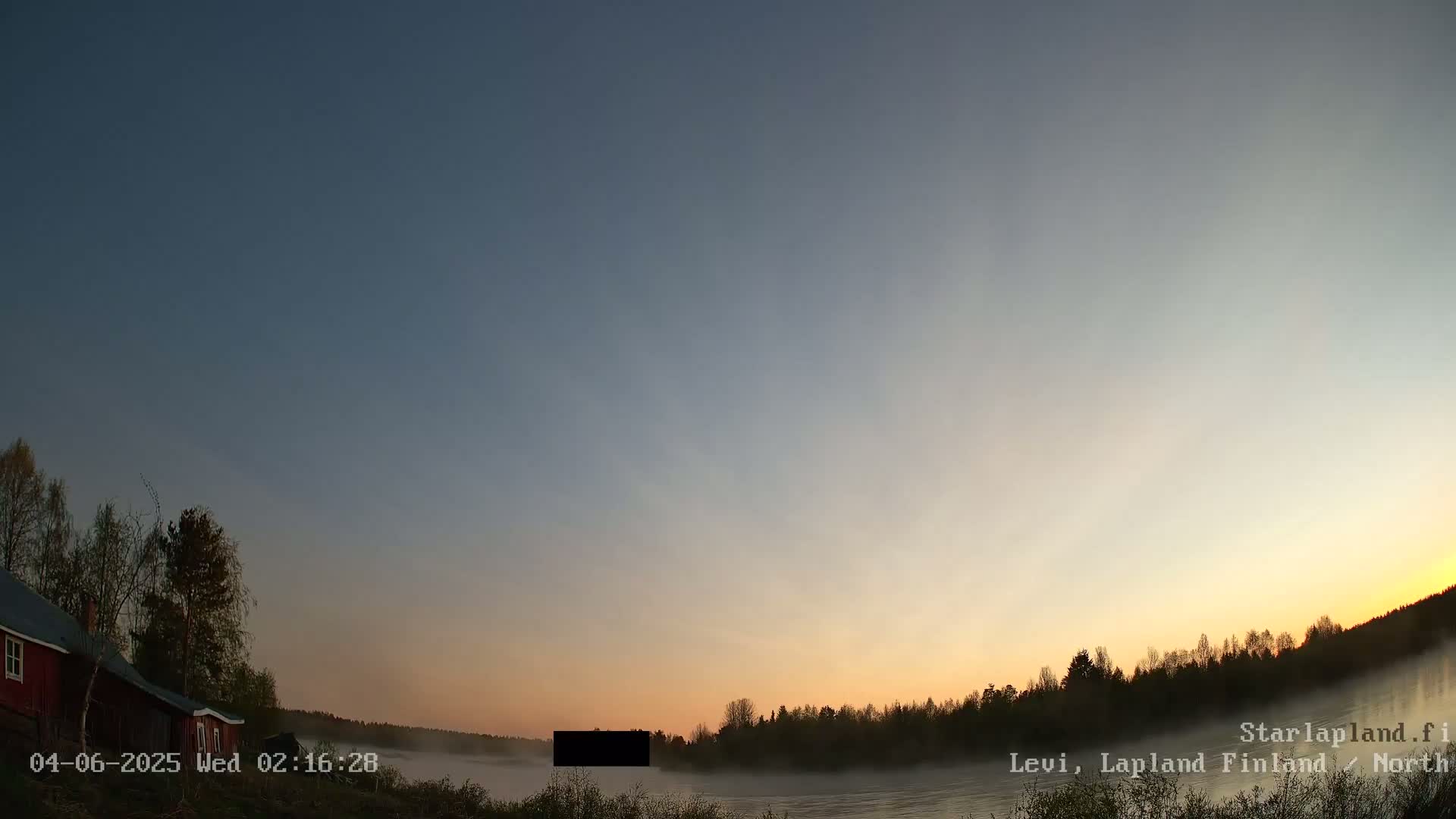 A red house sits near a body of water covered in fog at sunrise under a clear, twilight sky.