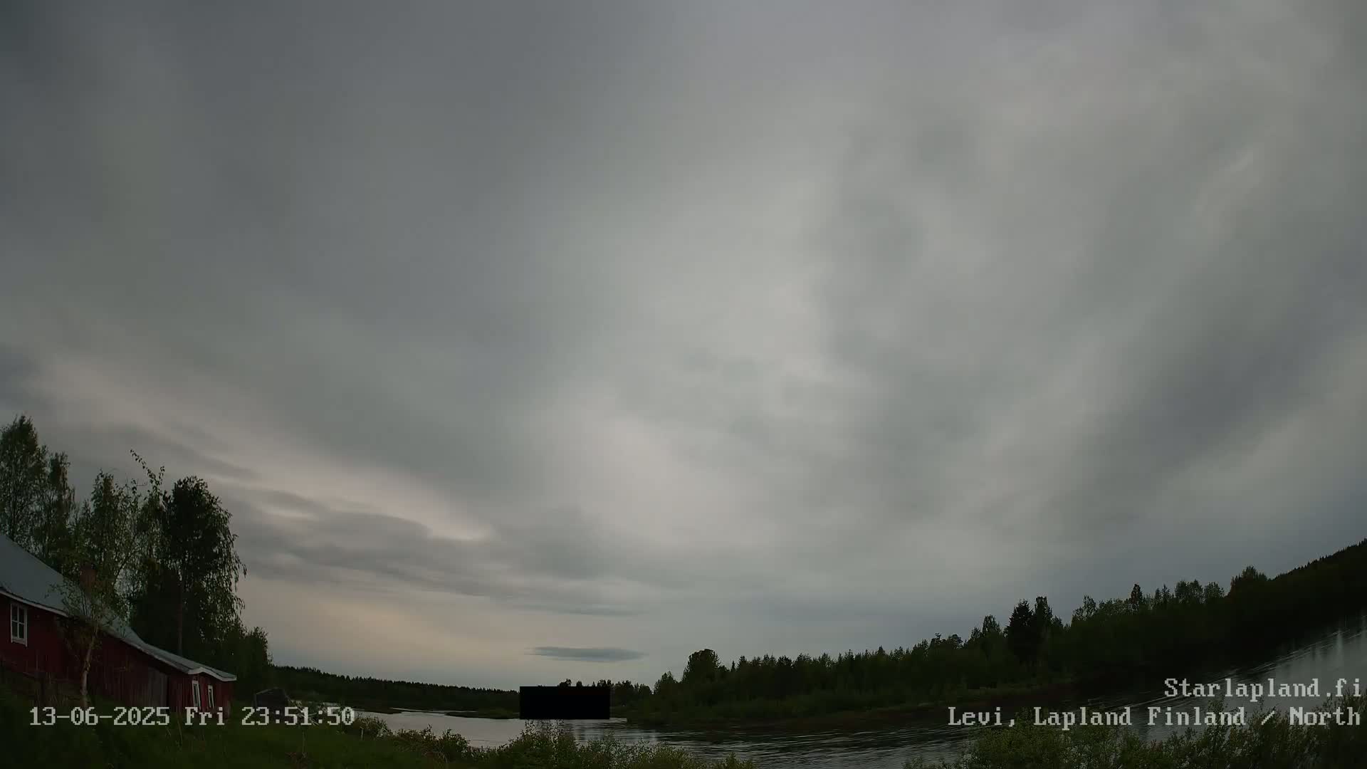 A red cabin sits near a calm river under an overcast sky.