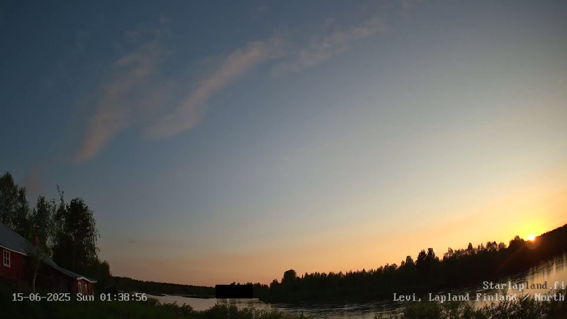 A mostly cloudy, overcast sky hangs over a calm river bordered by dark trees and a small red house.