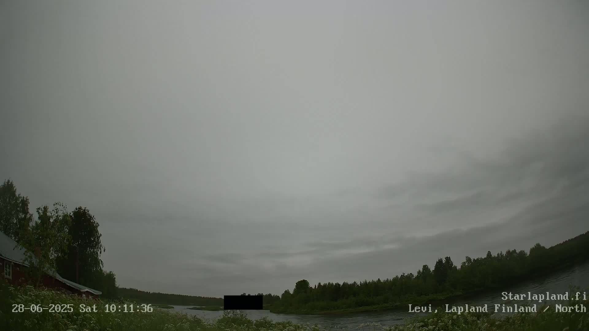 A mostly overcast sky hangs over a calm river, bordered by dark green trees and a small red house.