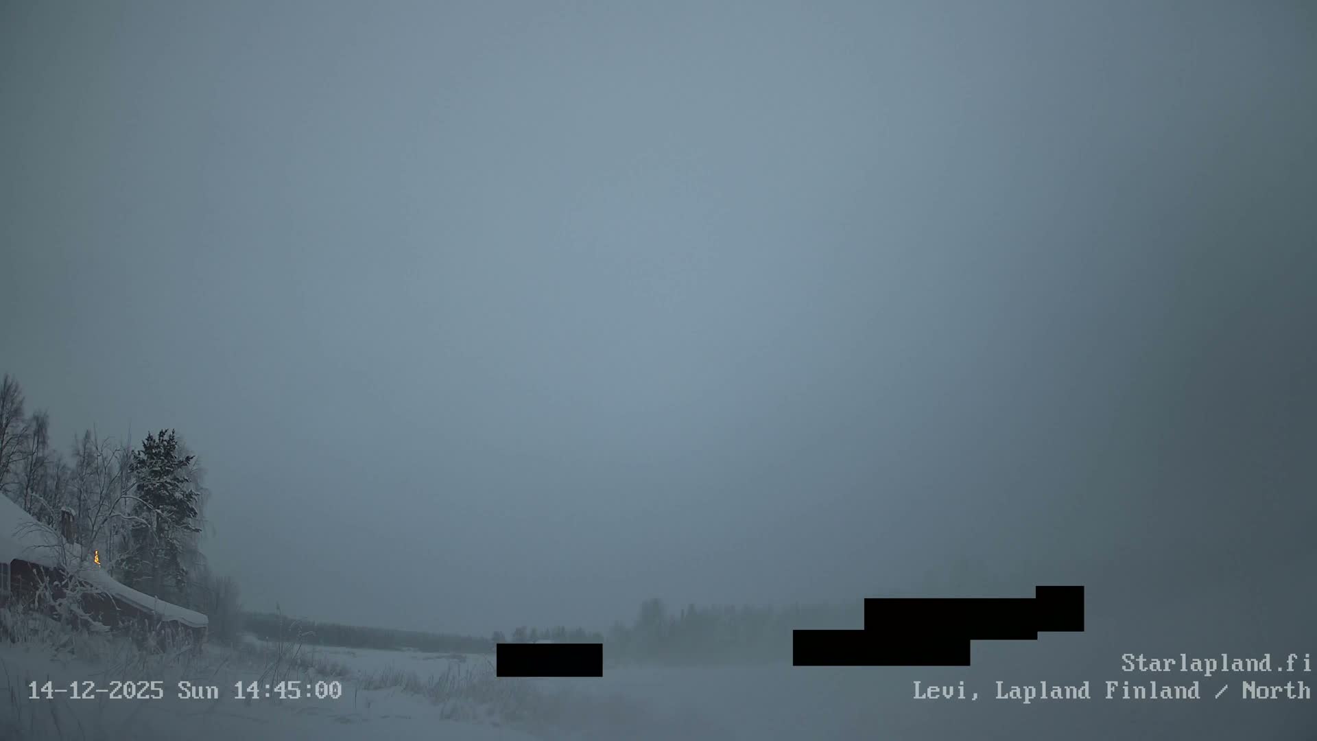 A wide, wintry landscape features snow-covered ground, frosted trees, a partially frozen body of water, and a red cabin on the left under an overcast, grey sky.