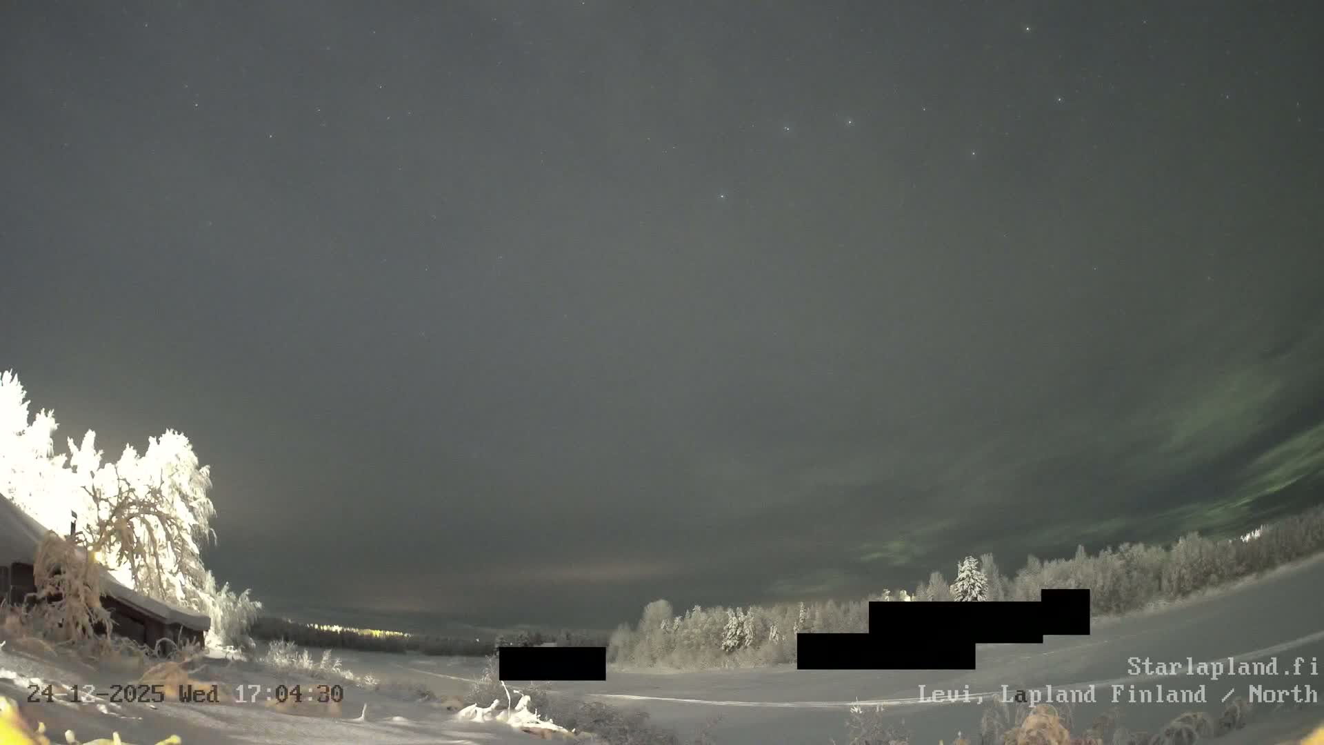 A wide, wintry landscape features snow-covered ground, frosted trees, a partially frozen body of water, and a red cabin on the left under an overcast, grey sky.