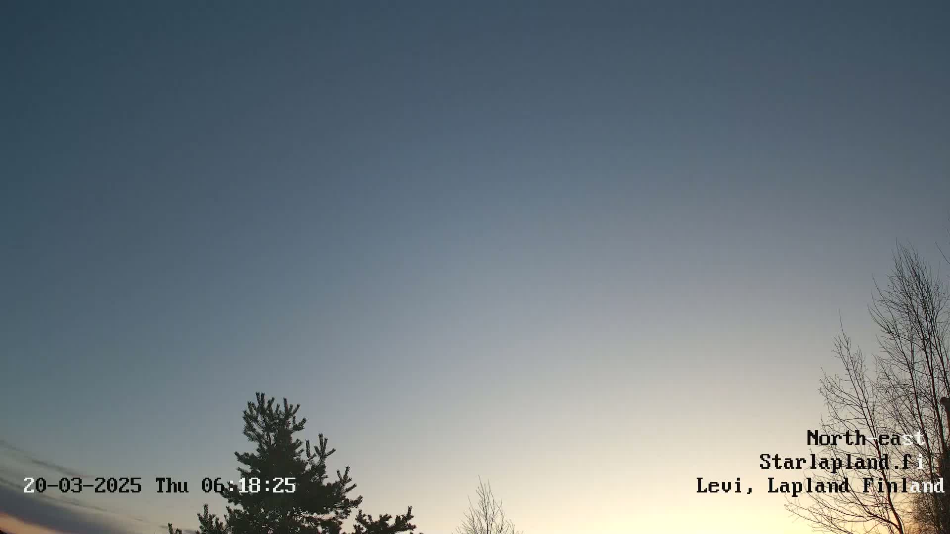 A twilight sky with a mostly clear, pale blue and orange gradient, and bare branches of trees are visible in the foreground.