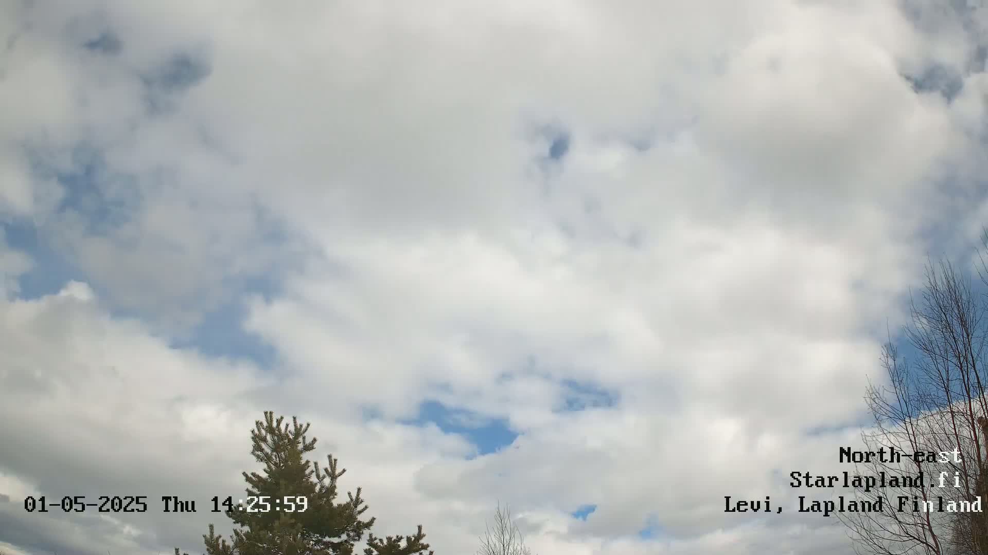 A mostly cloudy sky with patches of blue showing through, and some bare branches of trees visible at the bottom of the frame.