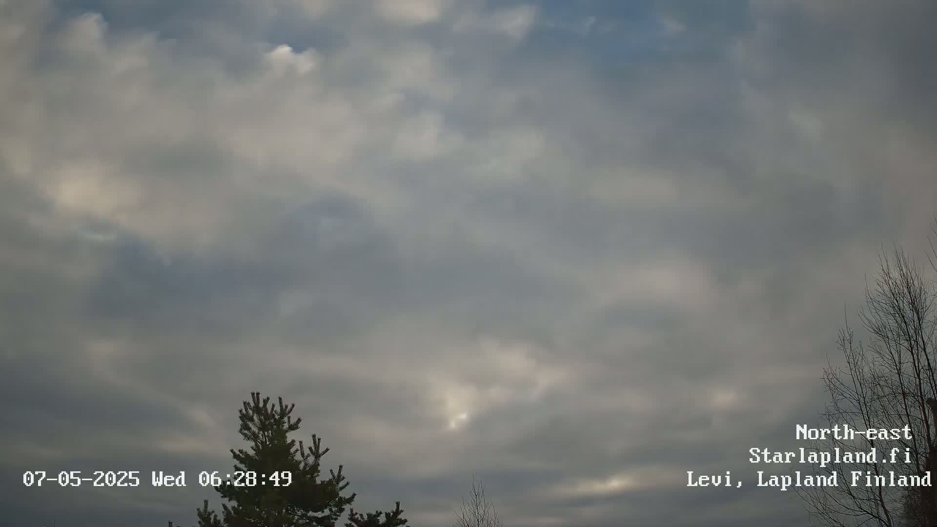 A mostly cloudy sky with some patches of brighter clouds is visible above a few silhouetted trees.