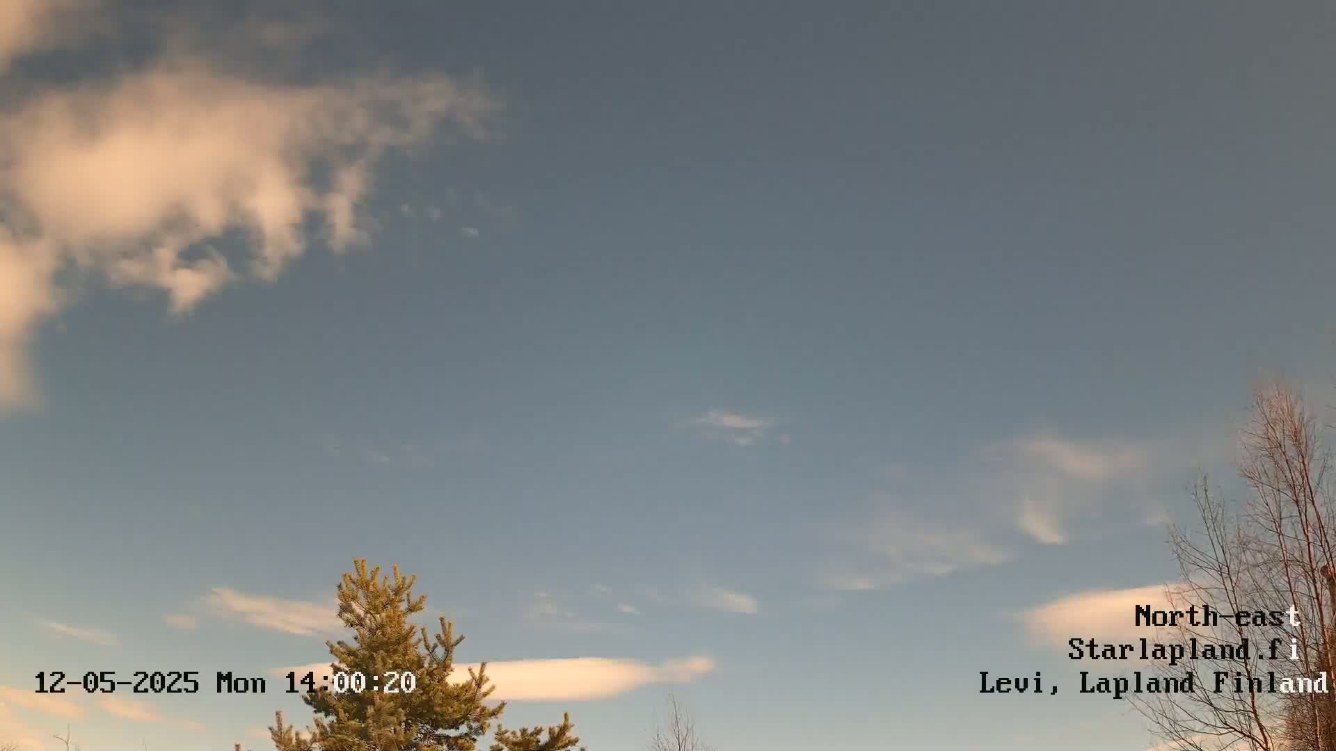 A mostly clear sky with a few wispy clouds and scattered trees is visible under a pale blue sky.