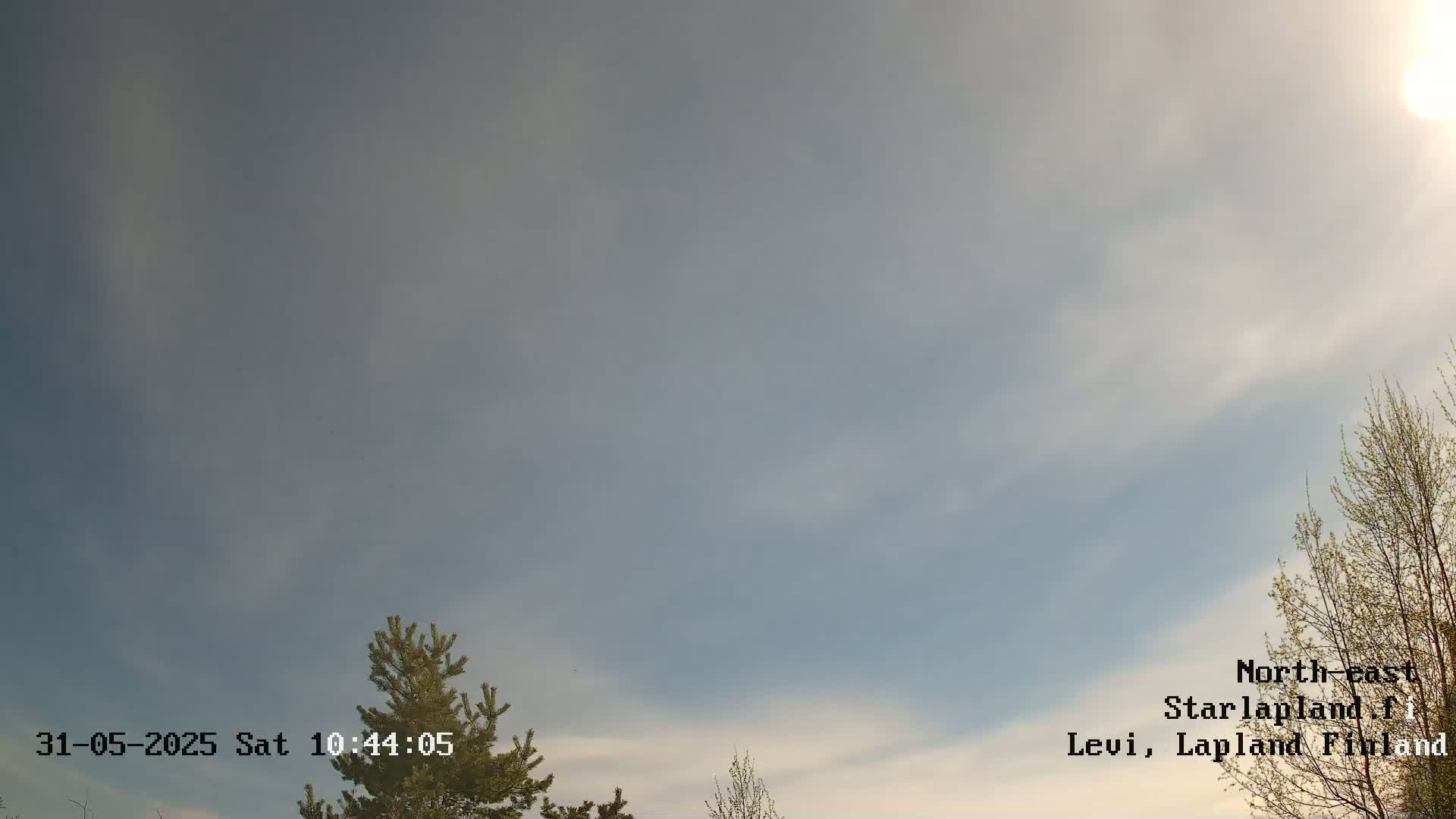 A mostly cloudy sky with hints of blue and sunlight, partially obscured by thin clouds, is visible above a few trees.