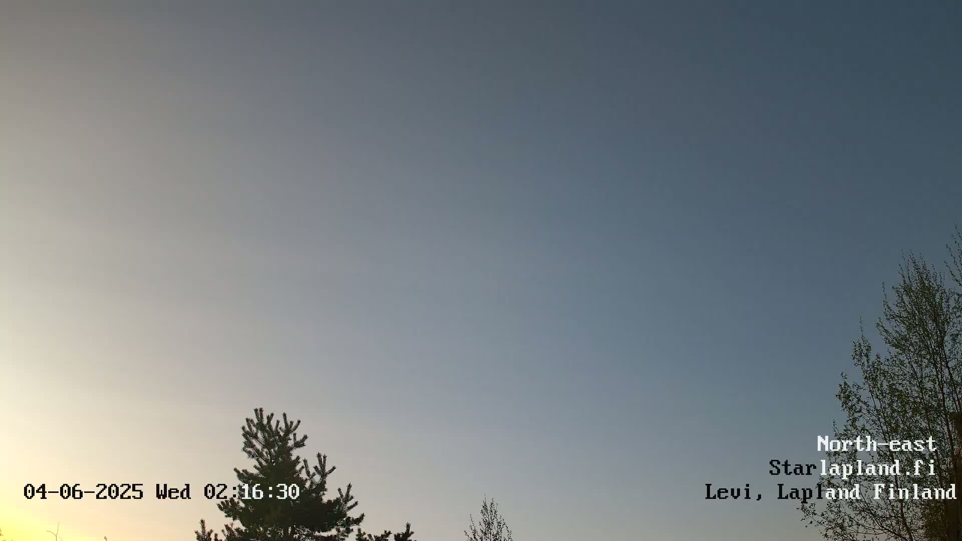 A clear, twilight sky is visible above a few silhouetted evergreen trees.
