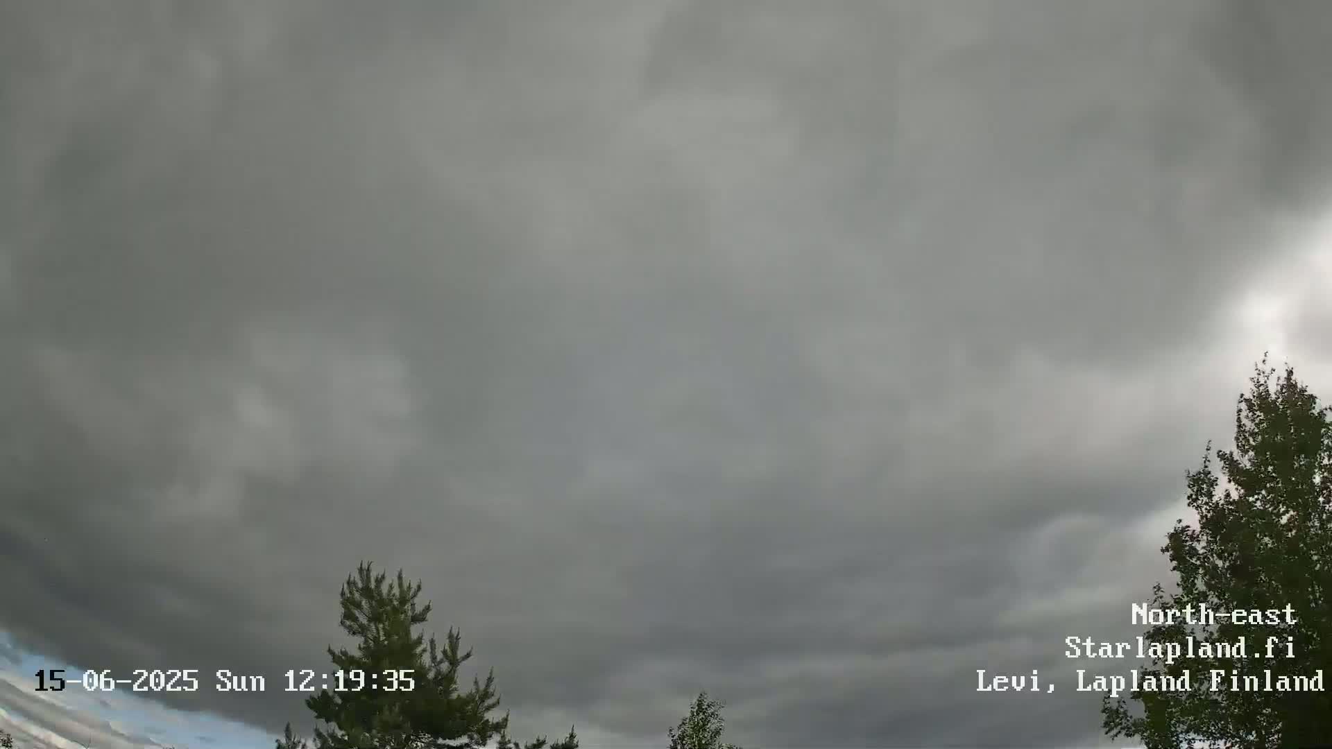 A mostly overcast sky with dark gray clouds hangs above some green trees.