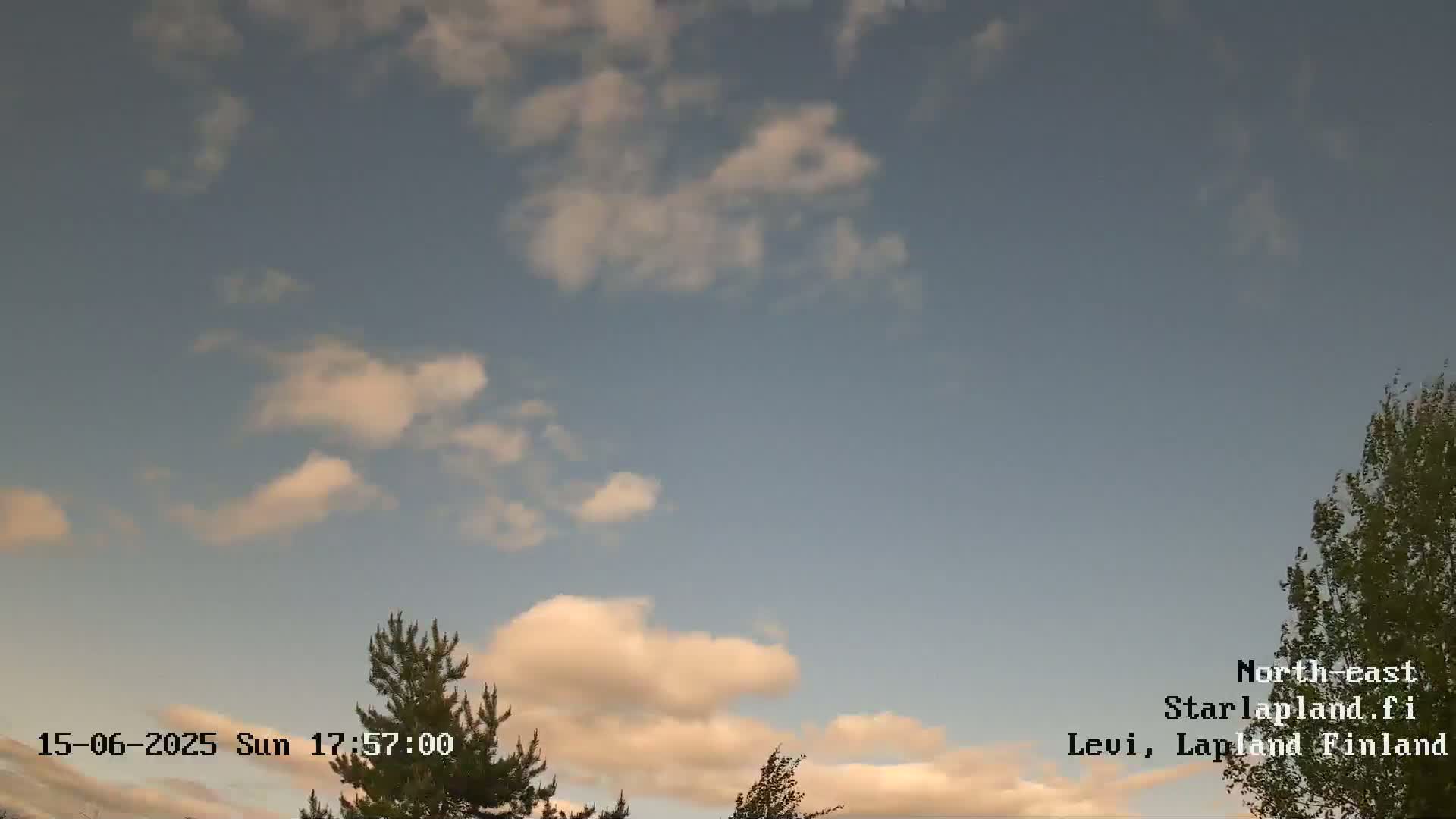 A partly cloudy sky with fluffy white and light peach-colored clouds is visible above some treetops.